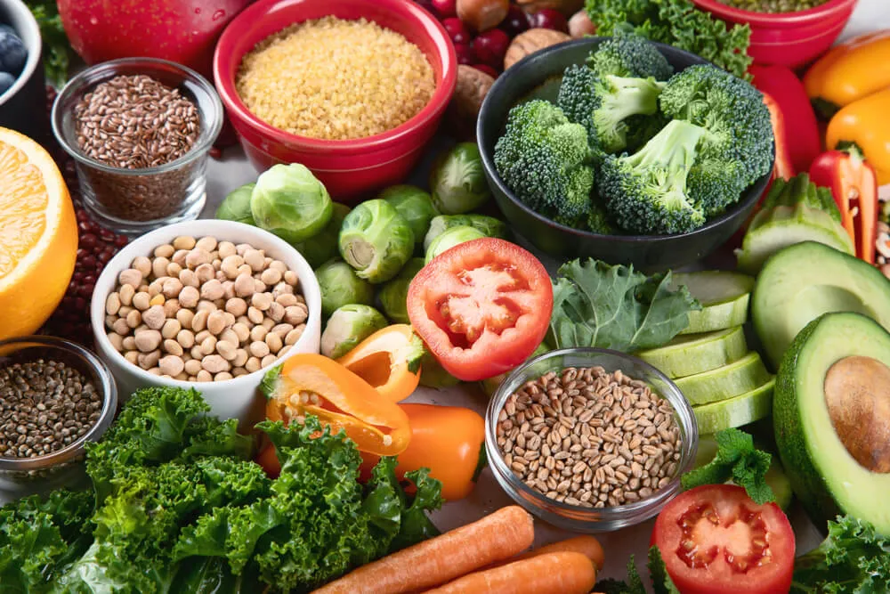 A bowl of dry dog food surrounded by various high-fiber ingredients like pumpkin, sweet potatoes, carrots, peas, and flaxseeds, emphasizing a balanced canine diet.