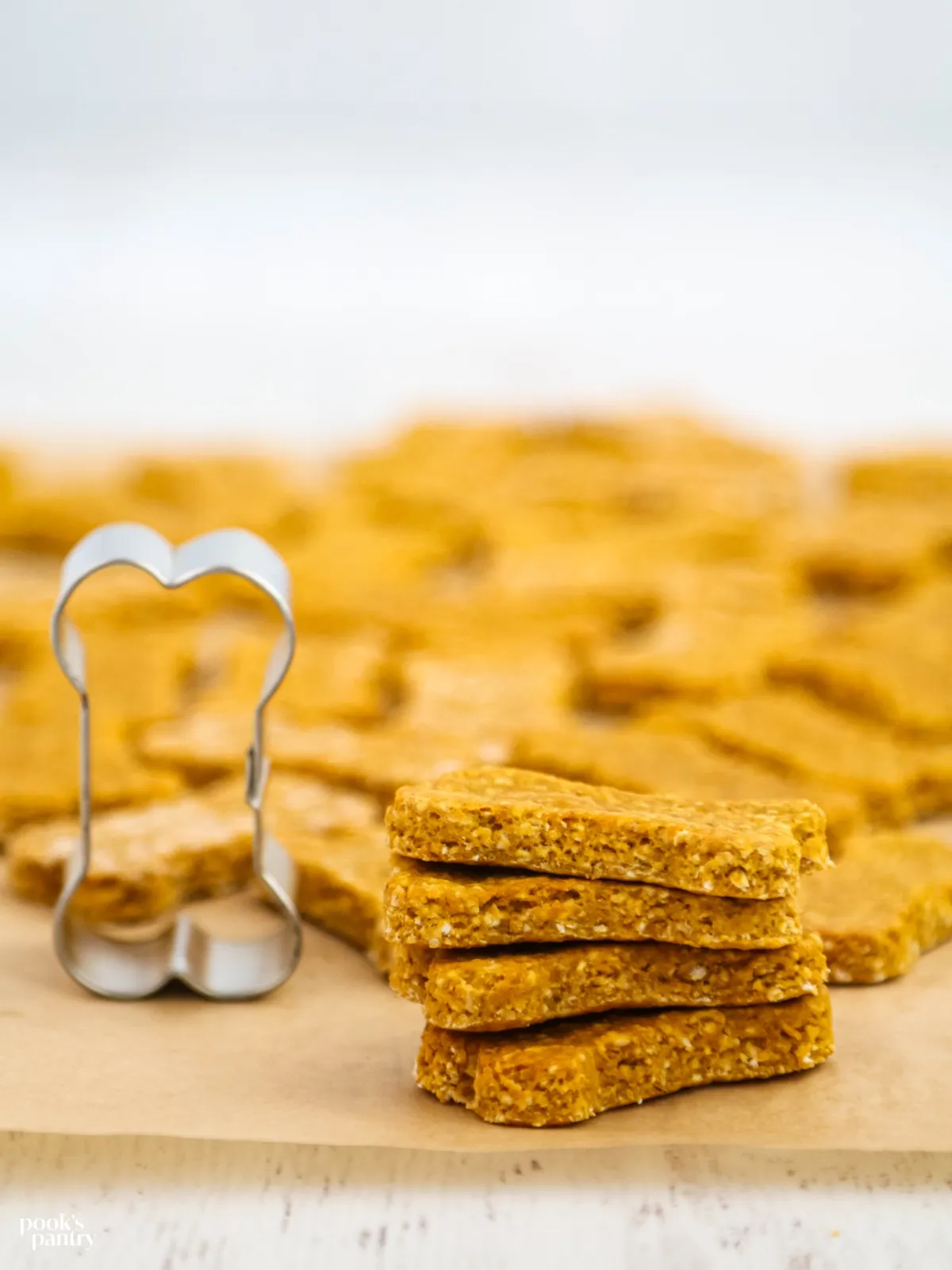 A collection of stacked dog treats next to a bone-shaped cookie cutter, symbolizing the DIY nature of the recipe.