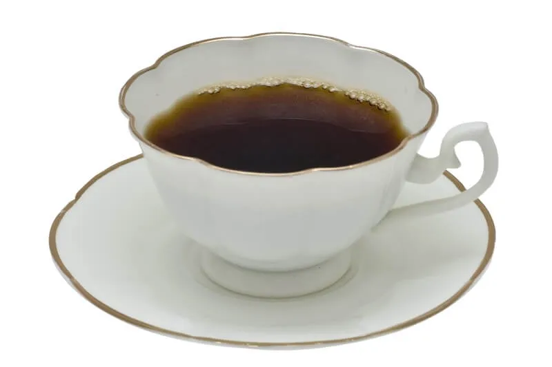 A cup of coffee with beans scattered around, highlighting the danger of caffeine for dogs.
