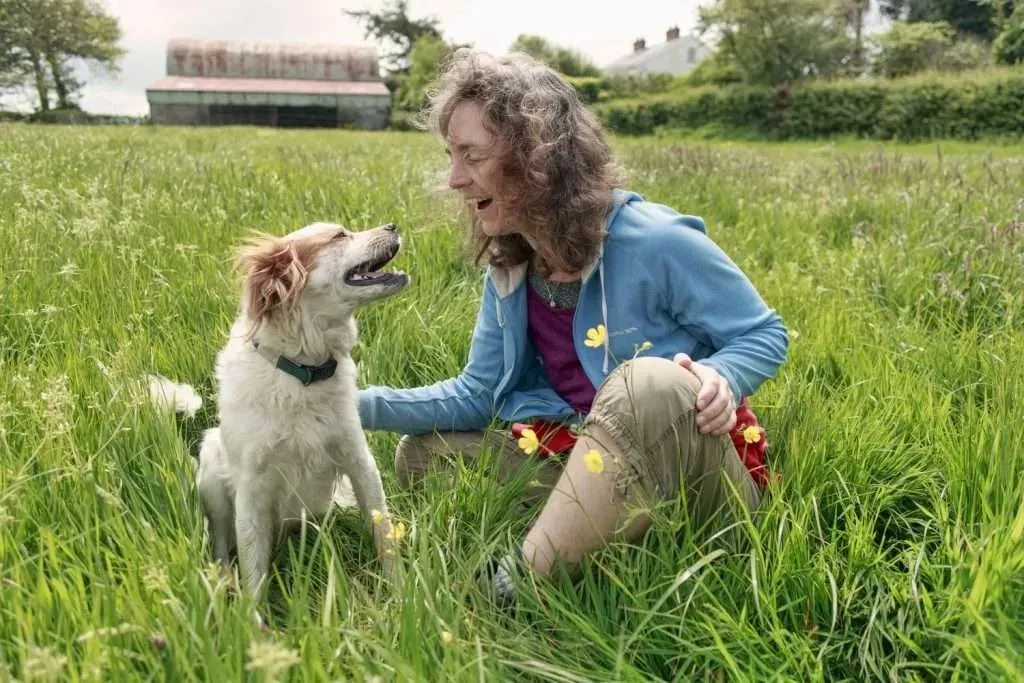 A dog and human sitting in a field of grass, looking happy