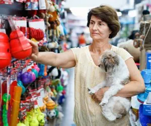 A person holding their large dog while carefully selecting the safest dog chews and toys from a display