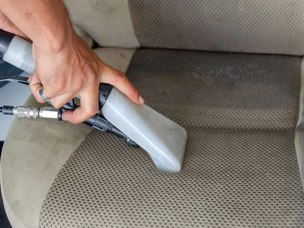 A person vacuuming dog hair from a car seat with a specialized pet hair attachment.