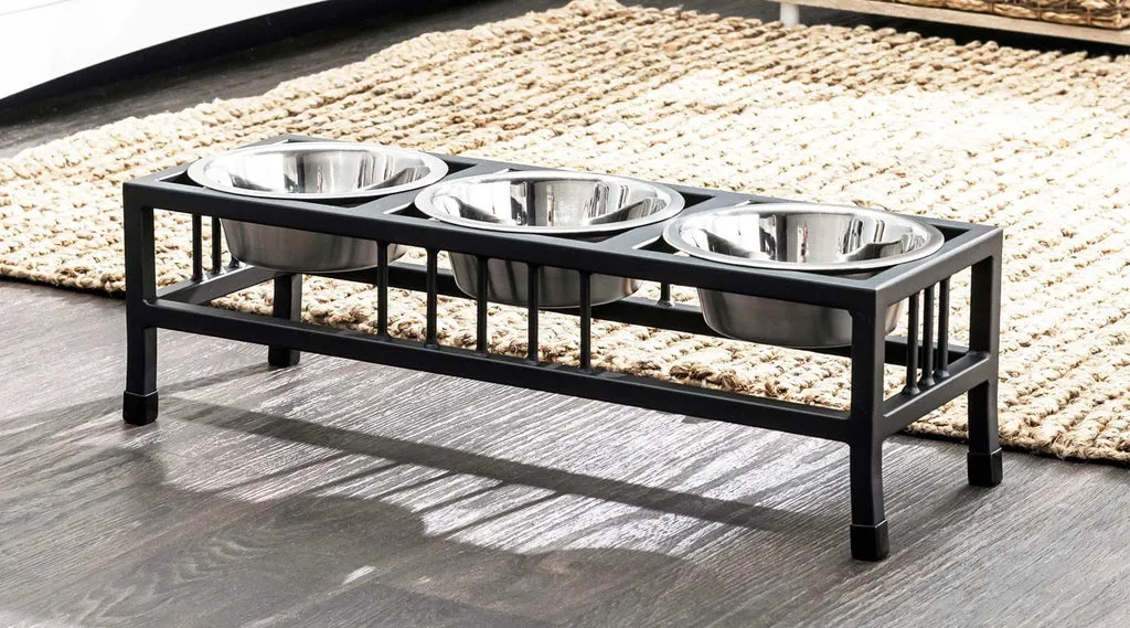 A stylish 3 bowl elevated dog feeder stand made of black wrought iron, holding three stainless steel bowls filled with dog food and water. A happy dog is seen eating from one of the bowls, demonstrating the convenience and health benefits.
