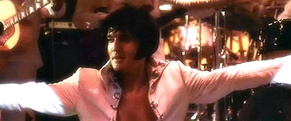 A wide shot of Elvis Presley captivating the audience on stage under dramatic lighting, illustrating the monumental impact of his 1970 Las Vegas concert documented in 'Elvis: That's The Way It Is 2001'.