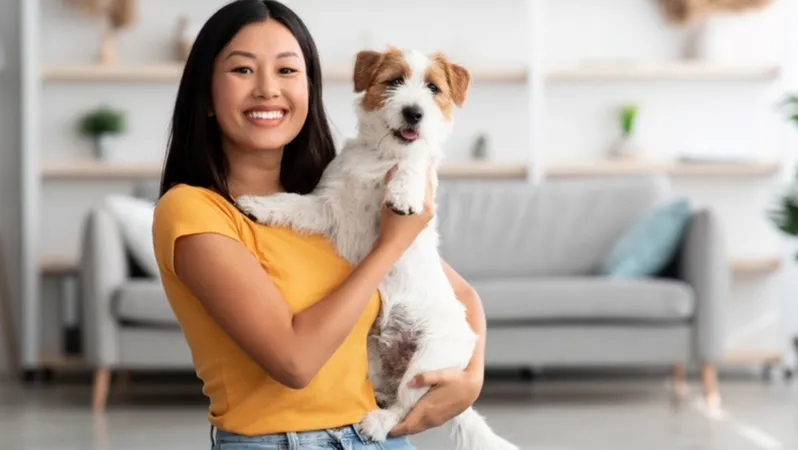 A woman gently holding a puppy while looking at the camera.