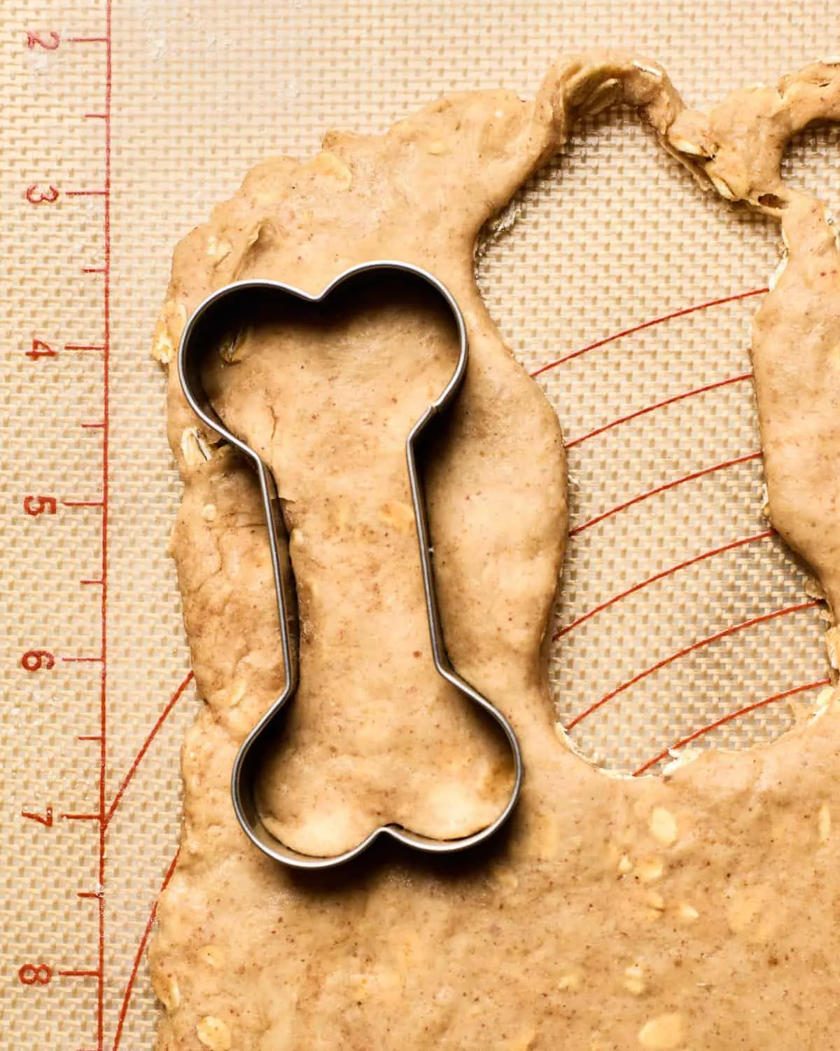 Dog treats being cut out of dough with a bone-shaped cookie cutter.
