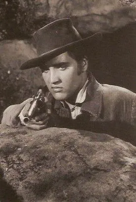 Elvis Presley as Clint Reno, looking intense with a pistol, in a scene from "Love Me Tender," showcasing his dramatic acting in his first movie role.
