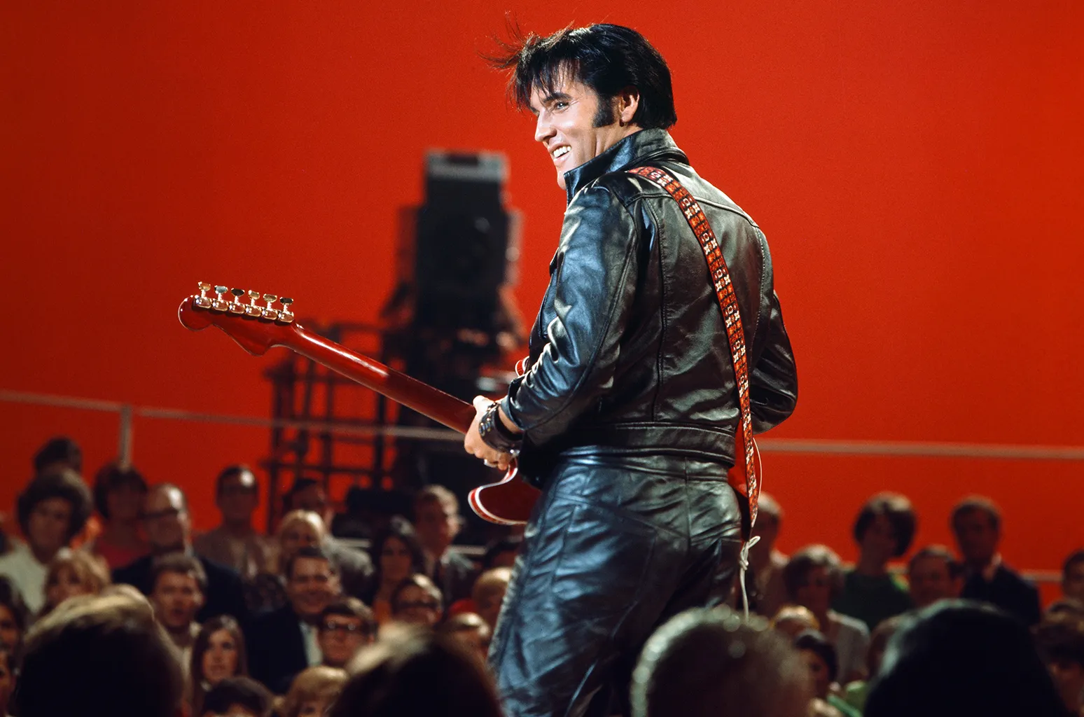 Elvis Presley performing with a red shirt and smile in 1968, embodying a classic rock and roll hit song