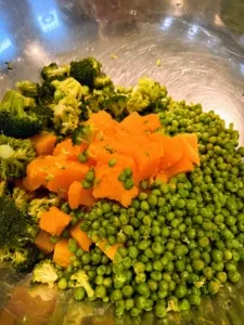 Frozen peas being added to a mix of cooked vegetables.