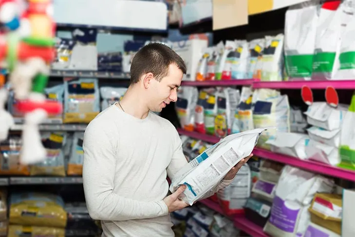 Man reading a food label on a bag of dog food at the store.