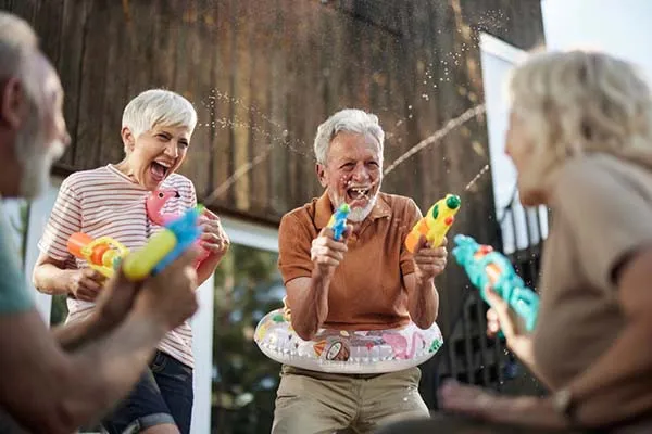 Photo of a group of senior women and men laughing and enjoying themselves while having a water gun fight on a patio
