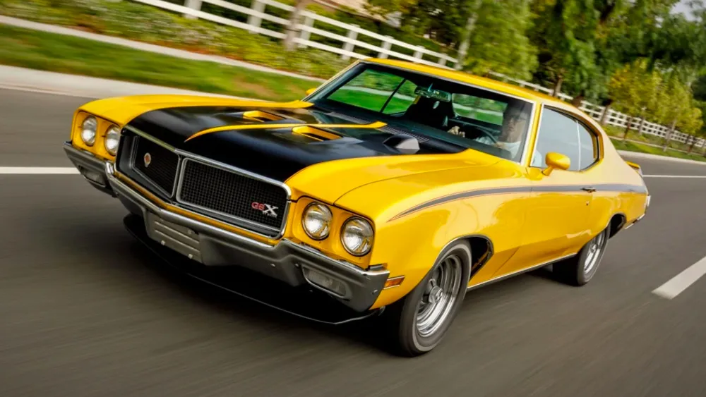 Side view of a bright yellow 1970 Buick GSX, featuring its distinctive black stripes and rear spoiler.