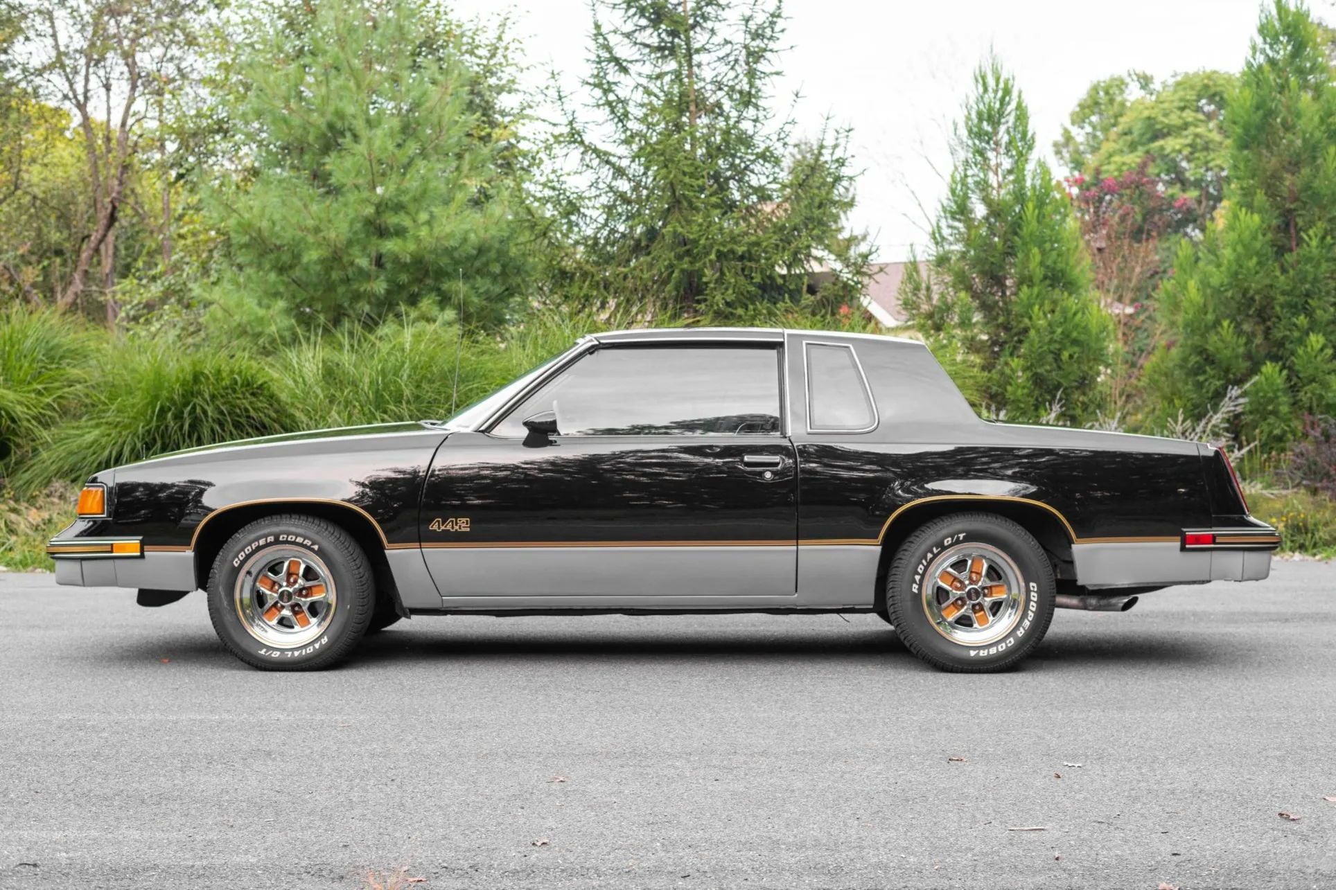The rear three-quarter view of a black and silver 1987 Oldsmobile Cutlass 442, showcasing the Super Stock III wheels and 442 trunk emblem