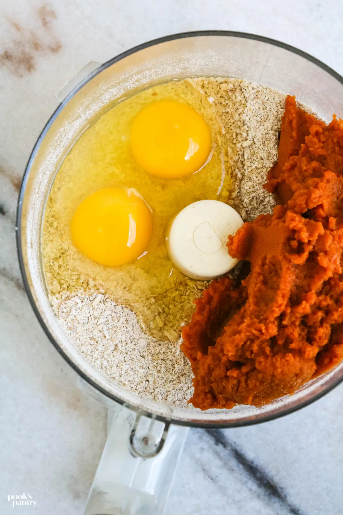 The three ingredients for the dog treat recipe are shown combined in the bowl of a food processor, ready for processing.