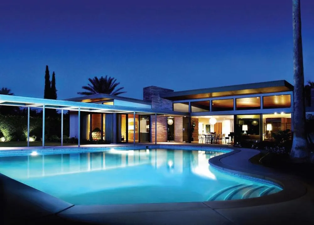 The Twin Palms estate illuminated at night, featuring the iconic twin palm trees where Frank Sinatra famously raised his Jack Daniels flag, beckoning celebrity guests.