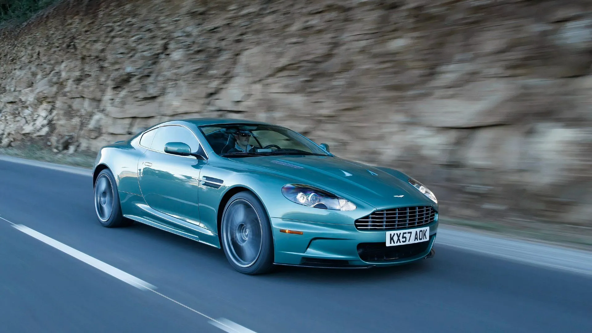 A 2008 Aston Martin DBS driving on a scenic road