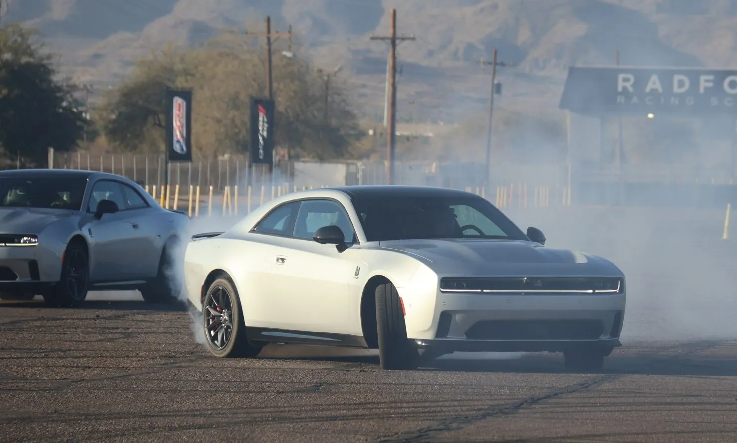 A 2024 Dodge Charger Daytona performing a controlled drift on a wet skid pad, with smoke from the tires
