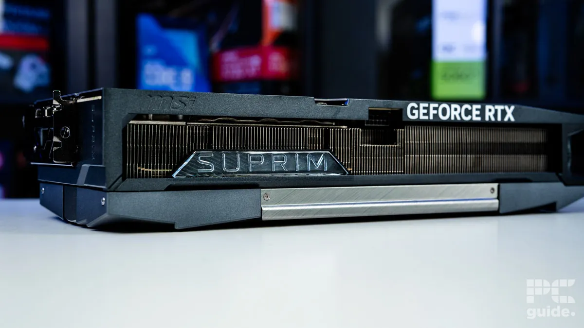 A background of blurred tech boxes sitting on bookshelves. The MSI Suprim SOC RTX 5090 sits on top of a white table. It