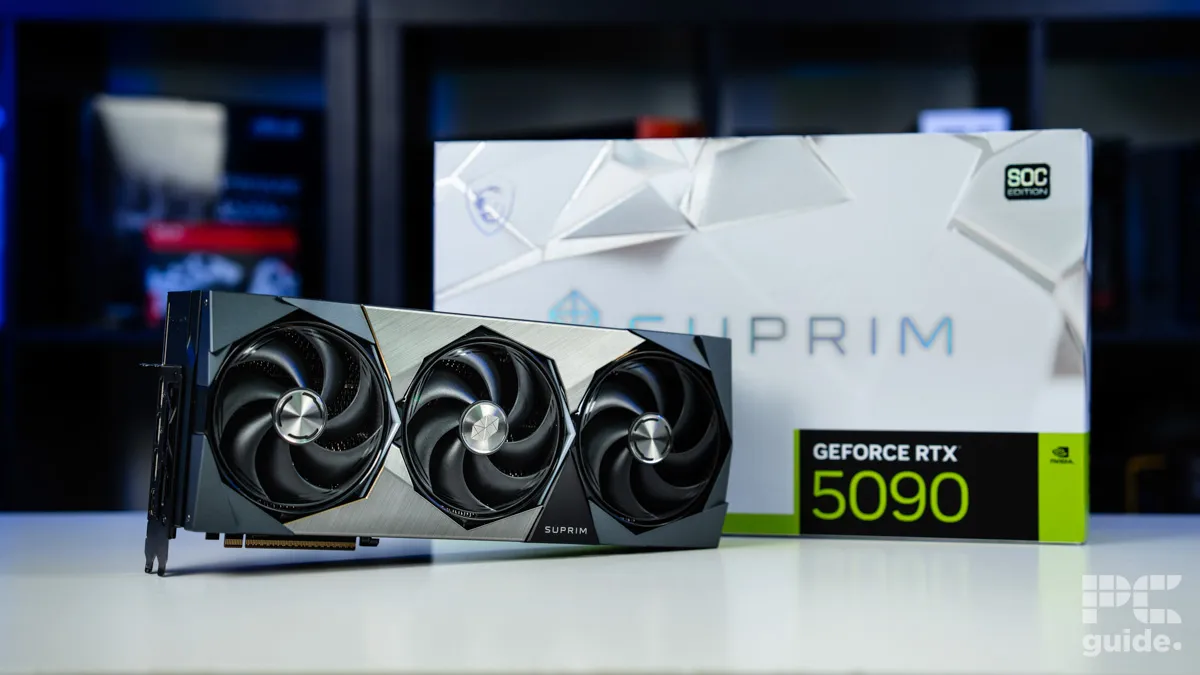 A background of blurred tech boxes sitting on bookshelves. The MSI Suprim SOC RTX 5090 sits on top of a white table, the fans pointing outwards. Behind it is the white box with th Suprim logo and RTX 5090 written on it.
