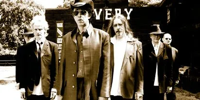 A black and white photo of a band member with a microphone, perhaps Rev. D. Wayne Love of Alabama 3