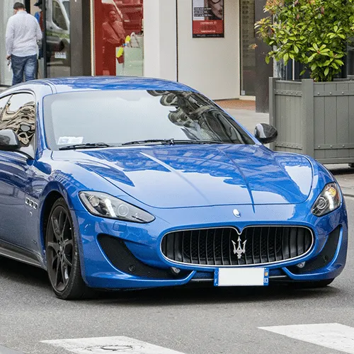 A dark blue Maserati parked gracefully by the water, highlighting its sleek lines