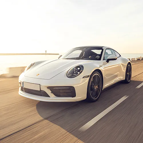A dynamic shot of a white Porsche 911 on a winding road with mountains in the background