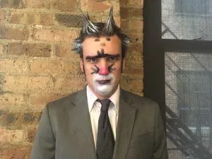 A person in a suit with cat-like makeup and ears, portraying the Split the Room host.