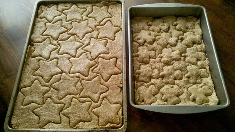 A person's hands are shown pressing the thick, sticky spent grain and peanut butter dough onto a baking sheet, preparing it for scoring and baking.