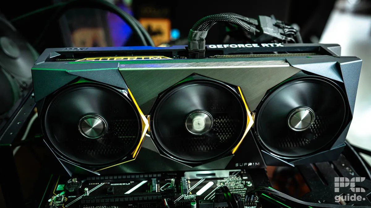 A silver GeForce RTX graphics card plugged into a motherboard and turned on. The three fans at the front of the card are spinning with teh adapter cable coming out the top.