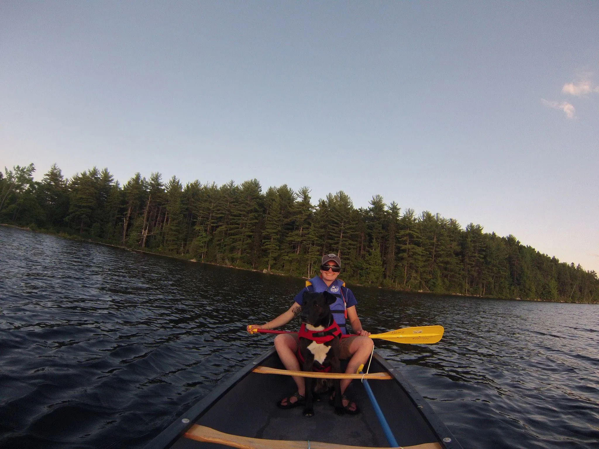 A woman and her dog sit in a canoe on a lake.