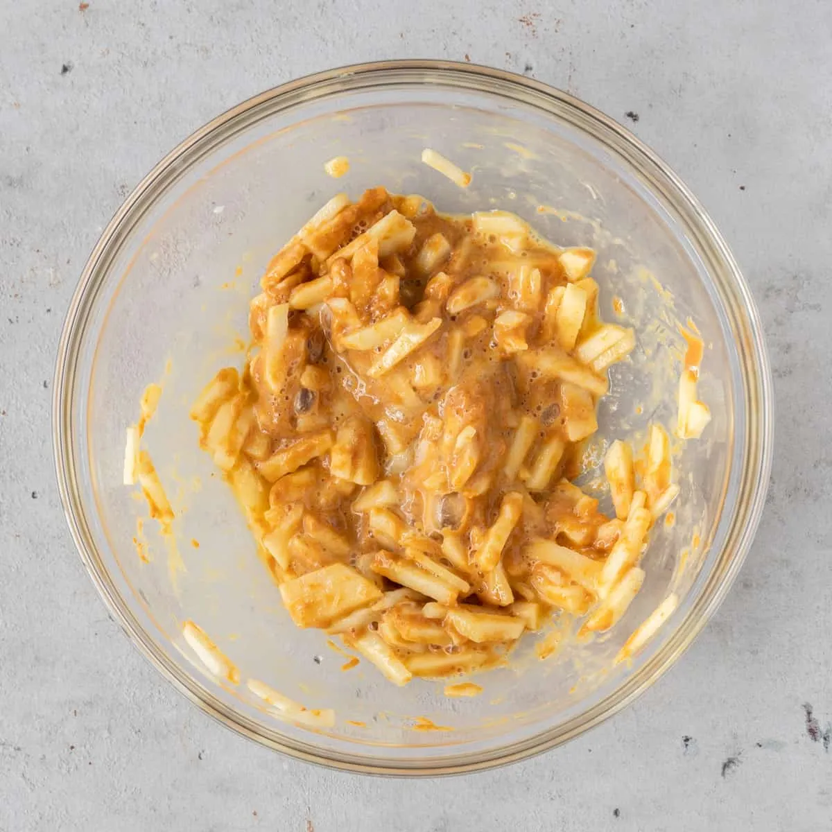 All the homemade dog cake ingredients – chopped apple, peanut butter, egg, and baking powder – thoroughly mixed together in a glass bowl, creating a thick batter.