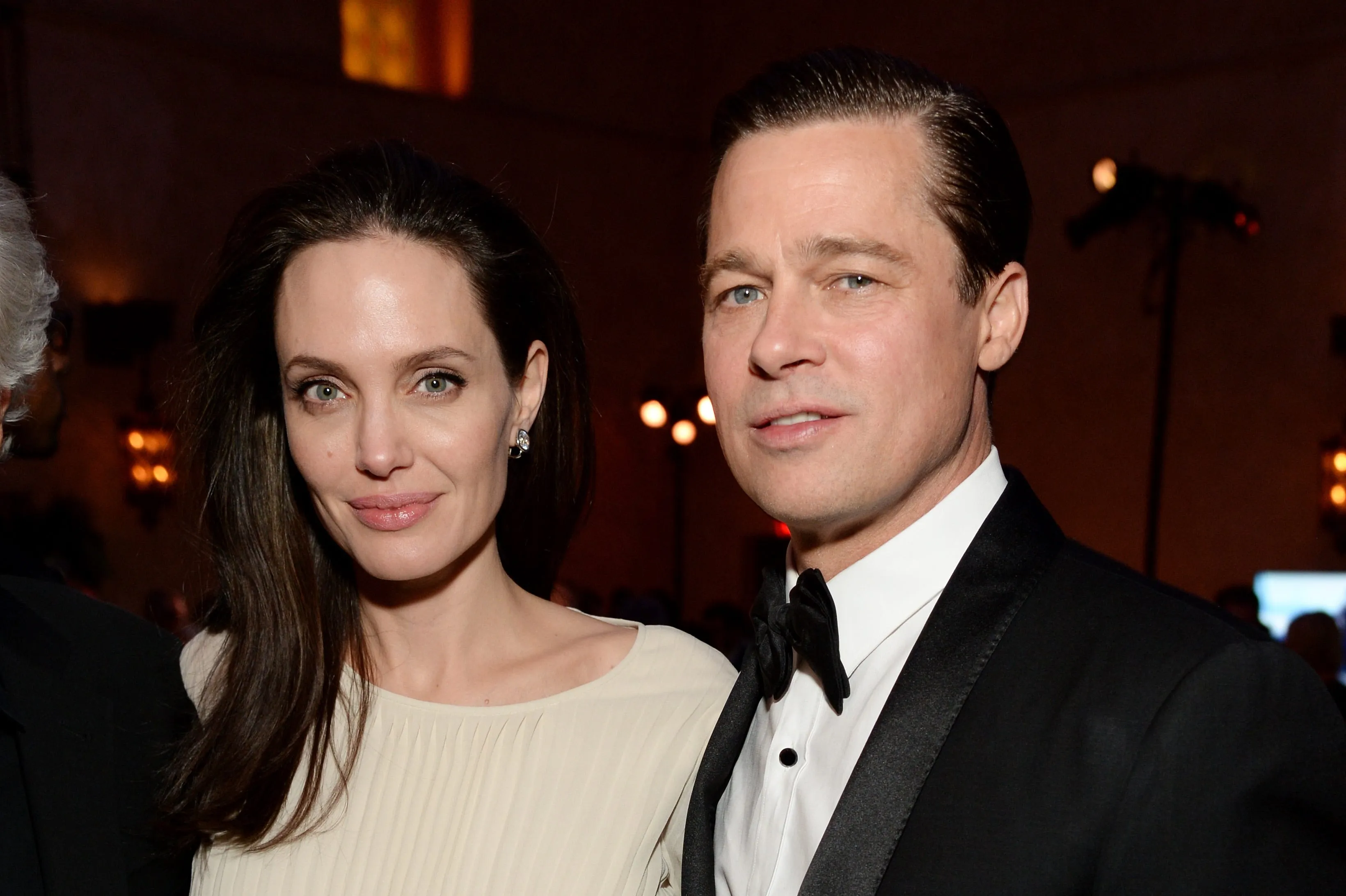 Angelina Jolie and Brad Pitt posing together, with Jolie in a cream-colored outfit and Pitt in a black tuxedo