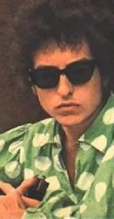 Black and white photo of Bob Dylan in a dark suit, leaning on a wall, looking thoughtfully into the distance.