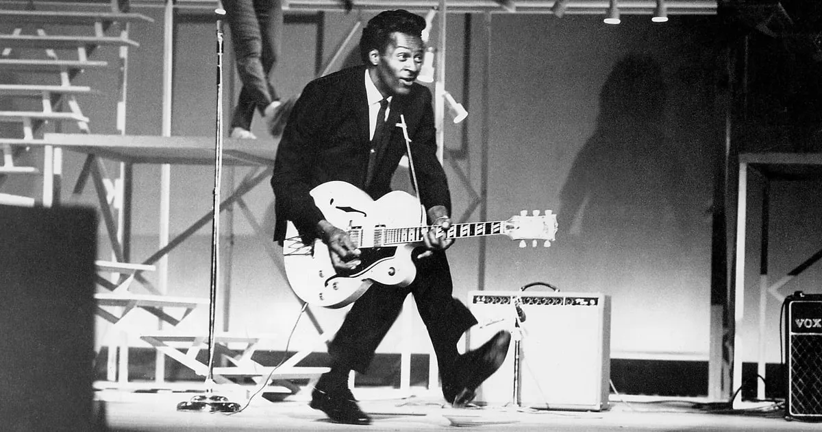 Chuck Berry performing his iconic duck walk with a guitar
