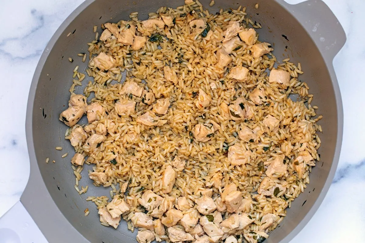 Cooked chicken, rice, and fresh parsley simmering in chicken broth in a large skillet.