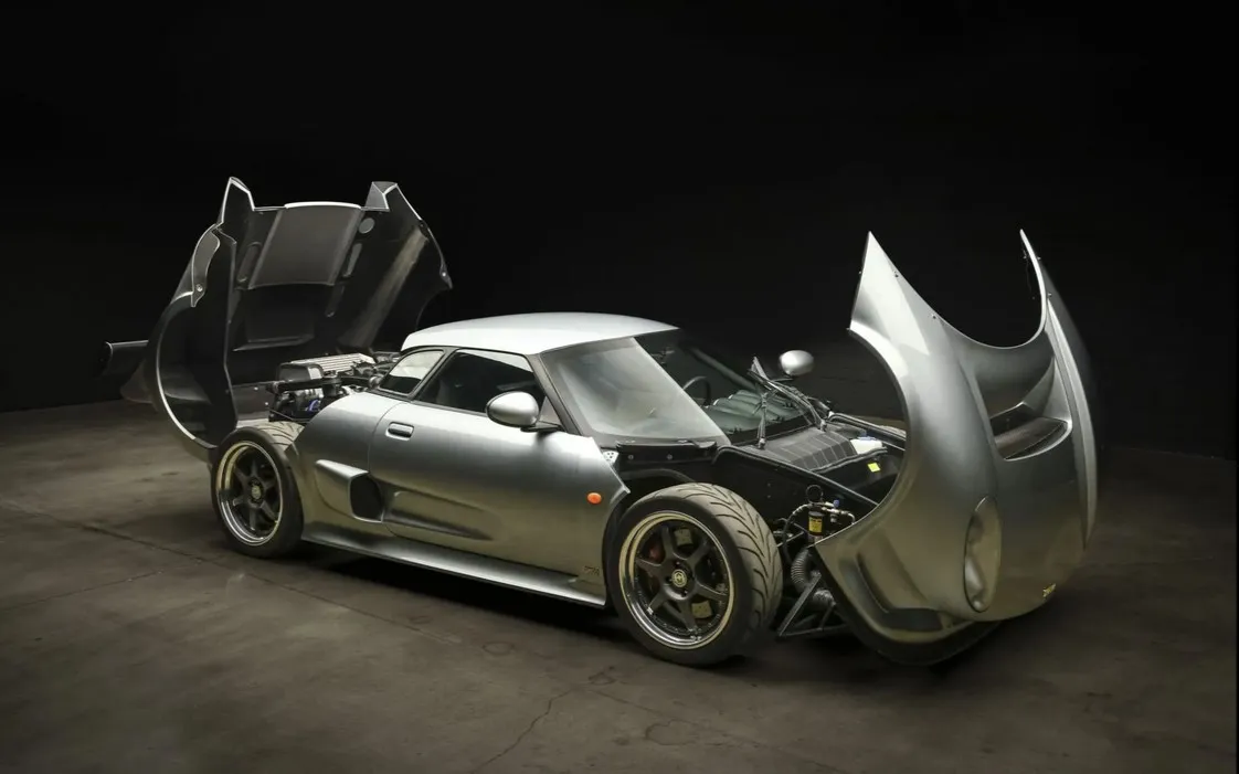 Front three-quarter view of a red 2006 Noble M400 parked outdoors, showcasing its distinctive headlights and aerodynamic profile