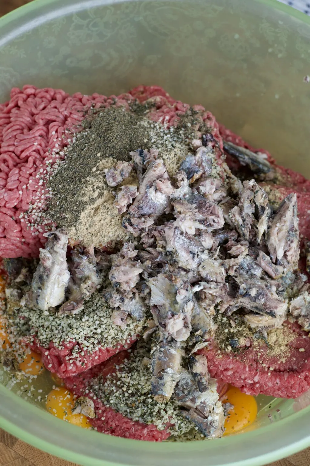 Mixing ground beef, eggs, kelp powder, ground ginger, hempseed, and sardines