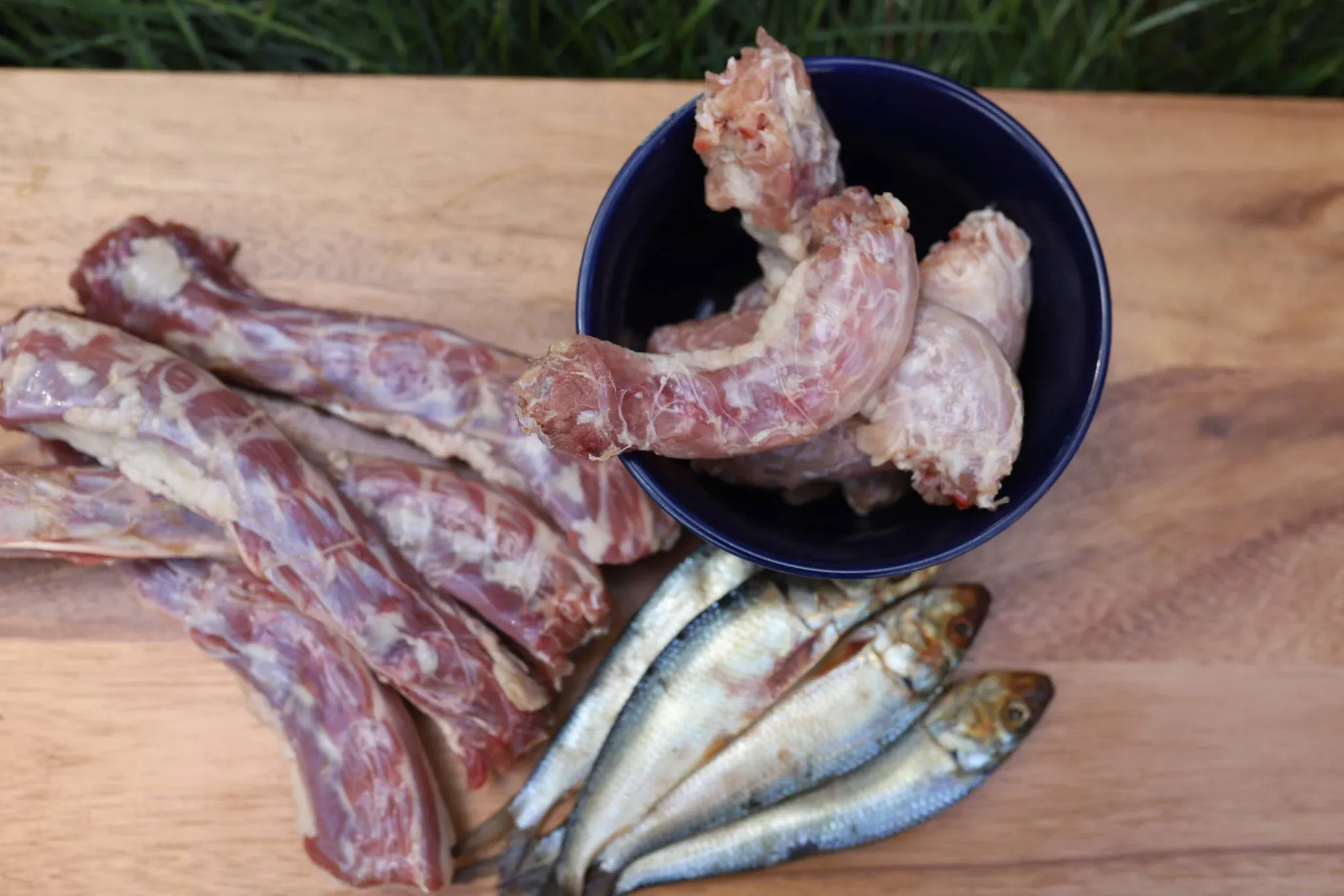 Raw chicken necks, turkey necks, and whole sardines on top of a wooden board.