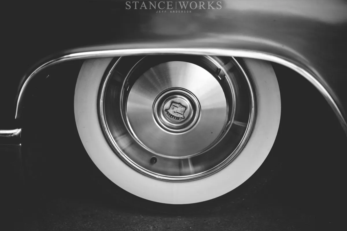Rear wheel of a 1966 Cadillac Coupe de Ville showing a classic hubcap and a wide whitewall tire