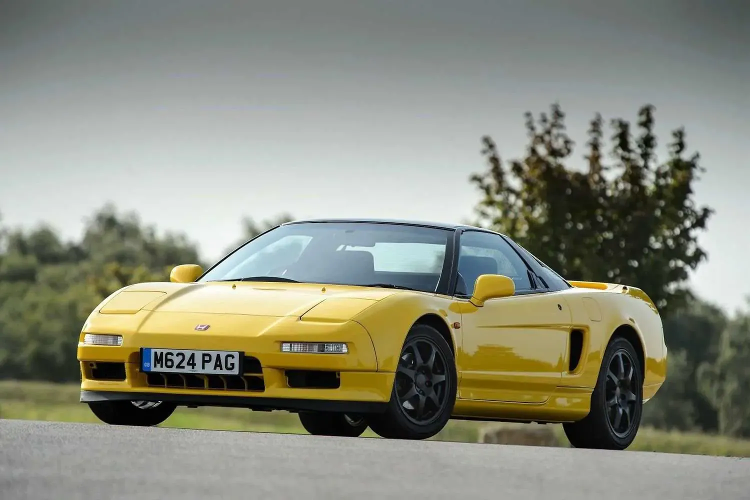 Red first-generation Honda NSX parked against a scenic background