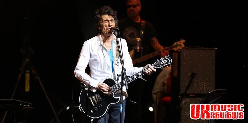 Ronnie Wood on stage with his band, surrounded by vibrant lighting during a captivating performance.