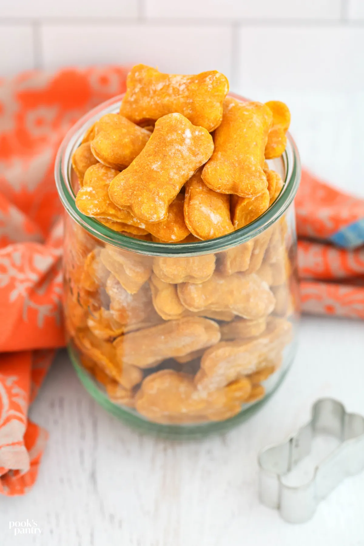 Soft pumpkin dog treats arranged in a glass jar, with a soft orange towel draped behind it, highlighting the treat's inviting texture.