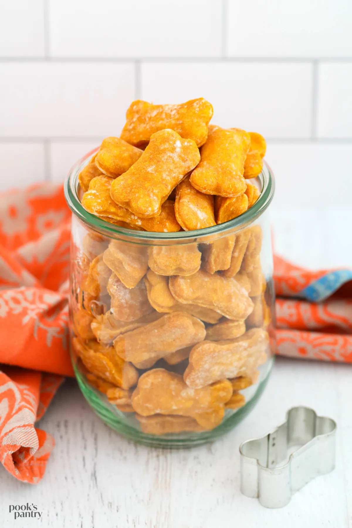Soft pumpkin dog treats in a glass Weck jar with an orange towel in the background.