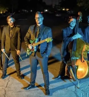 The Jazz Cartel performing live on stage with a spotlight on the lead singer and guitarist.