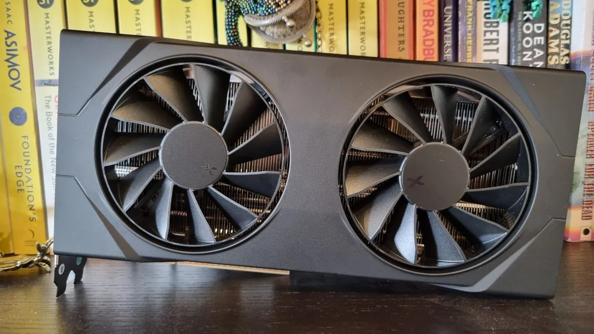 The XFX AMD Radeon RX 9060 XT graphics card resting on a set of bookshelves, surrounded by various books.