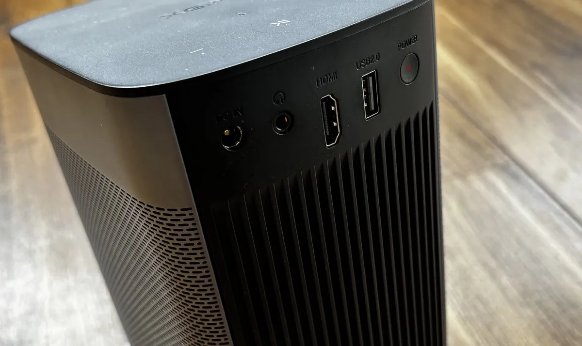 Xgimi Halo Plus mini projector in an outdoor setting at dusk, projecting a game onto a large screen