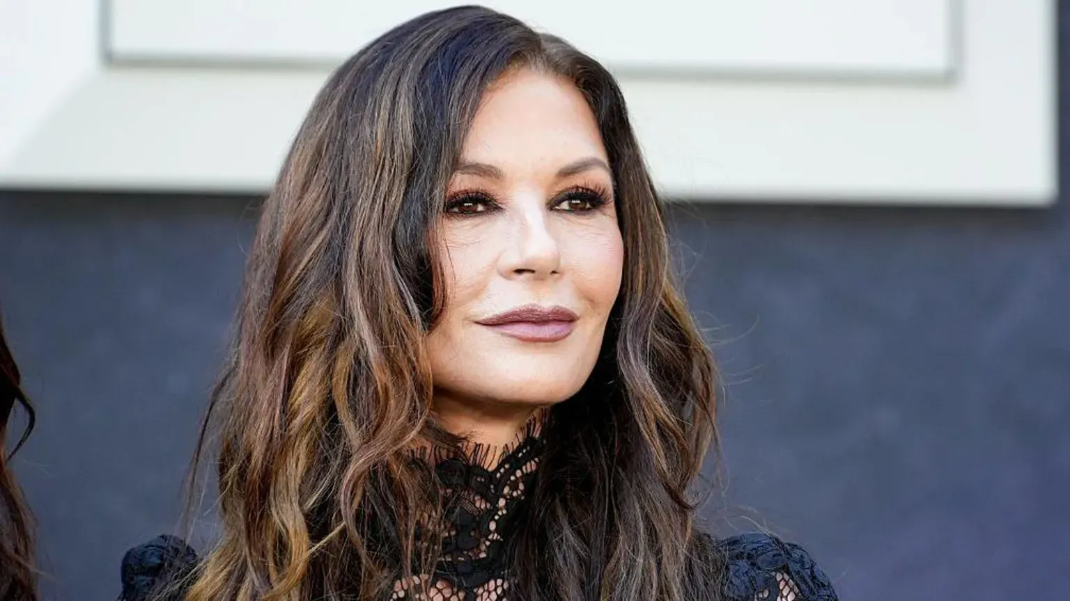 Close up of Catherine Zeta-Jones on the red carpet at the event. She has dark brown wavy hair and wears a black lace dress.