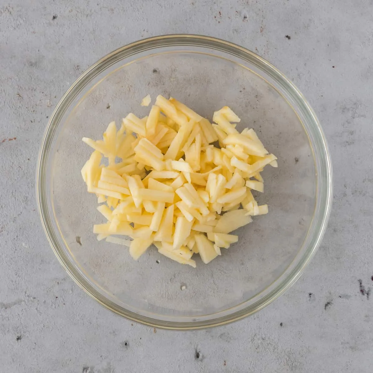 The chopped apple in a glass bowl on a grey background
