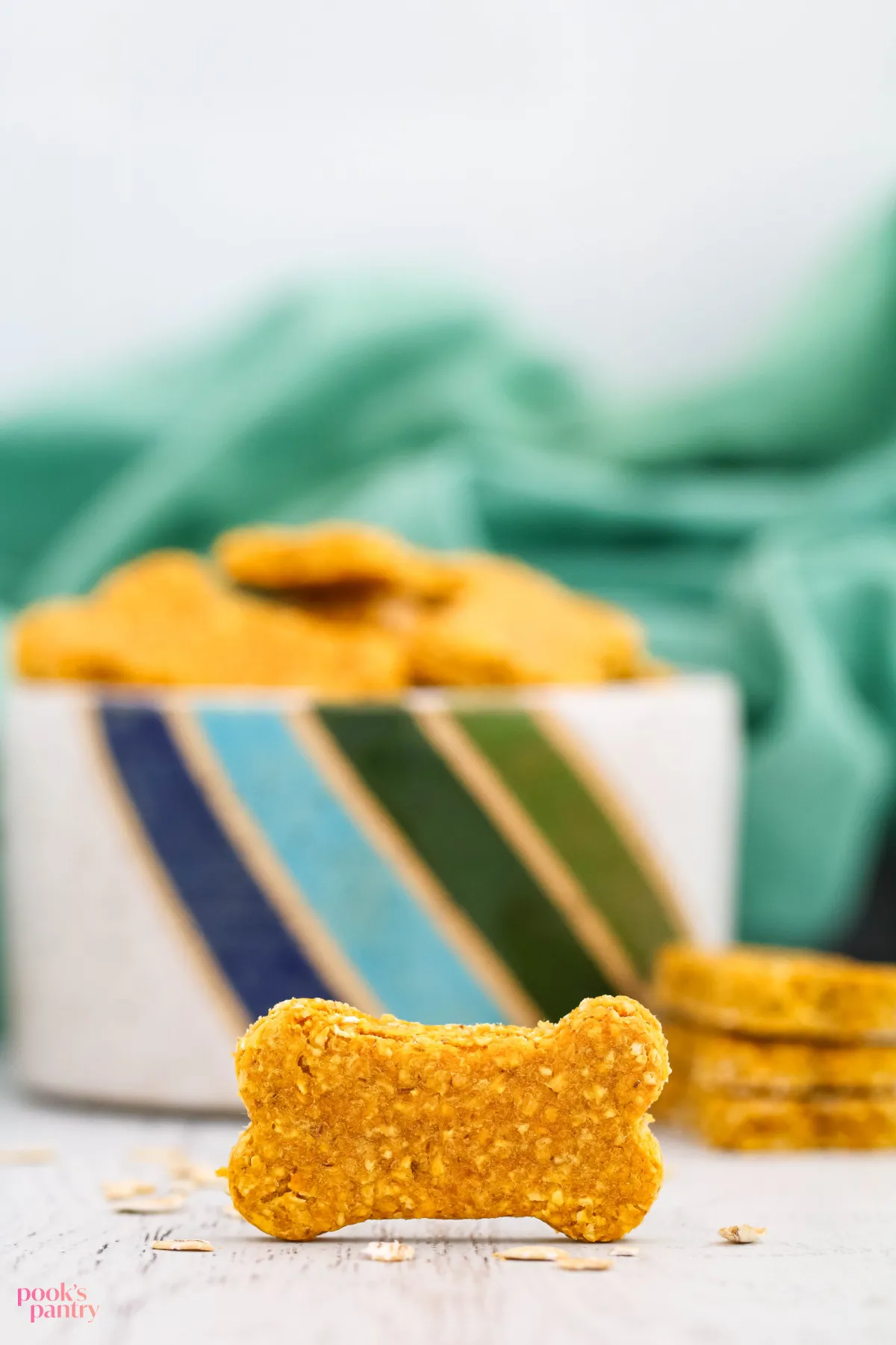 An oatmeal pumpkin dog treat standing on its side in front of a bowl full of dog treats.