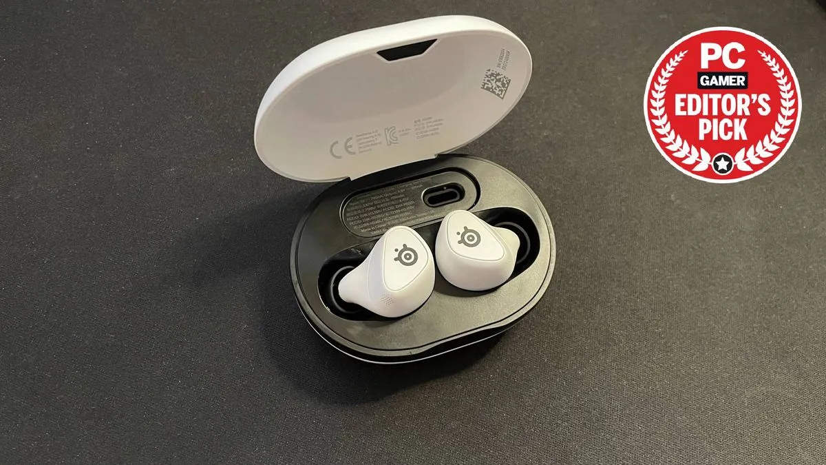 SteelSeries Arctis GameBuds in charging pod on a desk with the PC Gamer Editor